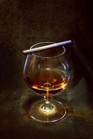 a glass of brandy and a cigarette in the background of brown suedeの写真素材