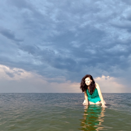 girl sitting on the surface of the water against the backdrop of a stormy skyの写真素材