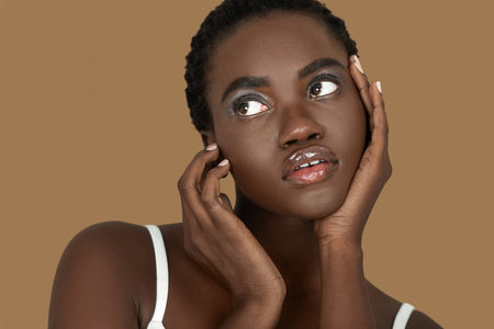 Closeup portrait of a cute young black woman with short Afro hair, light makeup and lipstick posing by herself inside a studio with a pecan background resting the palms of her handの写真素材
