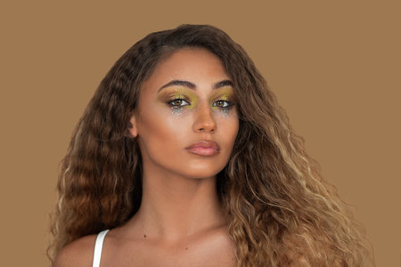 Closeup portrait of beautiful mixed race woman with long blond hair, eye makeup and lipstick posing by herself looking straight into the camera inside studio with pecan background.の写真素材