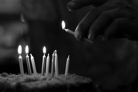Man Lighting Candles on a Birthday Cake in Black and Whiteの写真素材