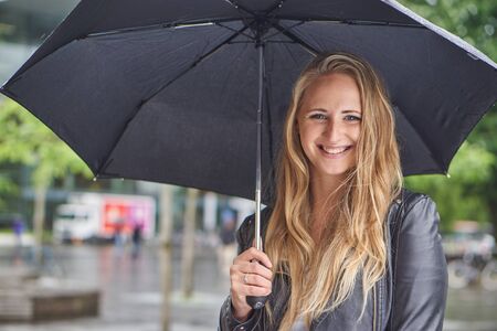 cute blonde woman with umbrella standing in cityの写真素材