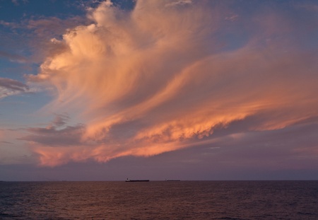 Brilliant copper coloured clouds at sea reflecting into the ocean with a ship on the horizon 