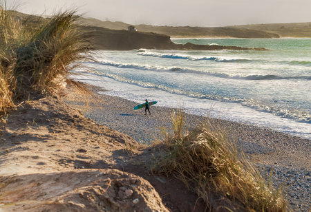 Surfer Leaving the Beach at Godrevy during Sunsetの写真素材
