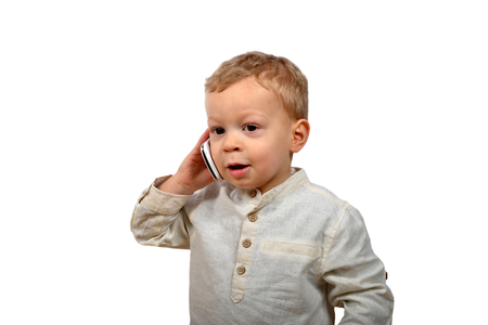 baby dressed in white speak with a mobile phoreの写真素材