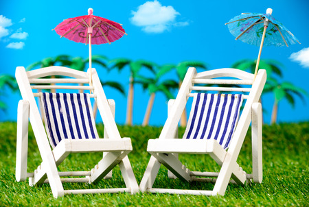 two small sun loungers on grass with palm treesの写真素材