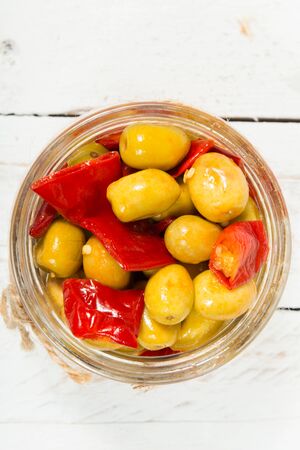 glass jar with olives and peppers on old white tableの写真素材