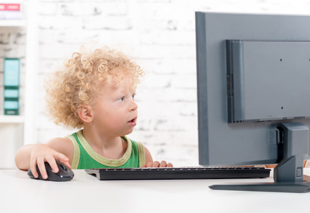 a small blond boy plays with a computer