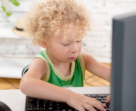 a little blond boy playing with the keyboard of a computerの写真素材