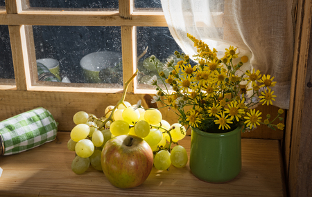 bouquet of wild flowers with grapes and an apple near a windowの写真素材