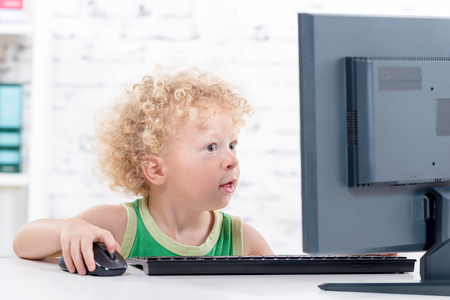 a little curly blond boy, plays with a computerの写真素材