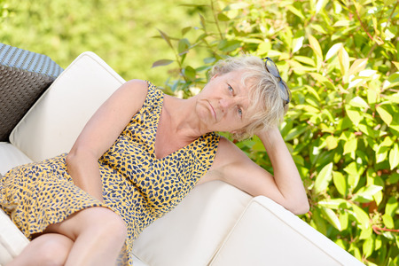 smiling blonde woman sitting on the sofa , in a gardenの写真素材