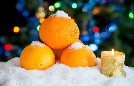 Three oranges in the snow with Christmas decor and bokehの写真素材