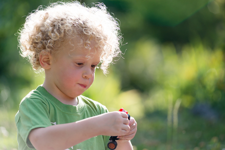 a small blond and curly boy playing with toy carの写真素材