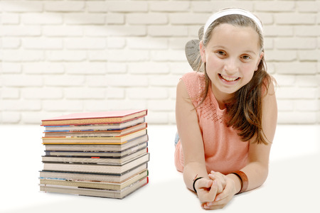 portrait of smiling little girl lying on the floor with several booksの写真素材