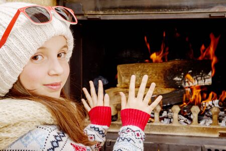 Winter at home, a pretty young girl sitting near the fire placeの写真素材