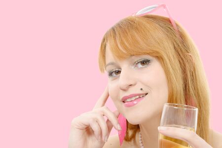 a pretty redhead woman drinks a glass of wine, pink backgroundの写真素材