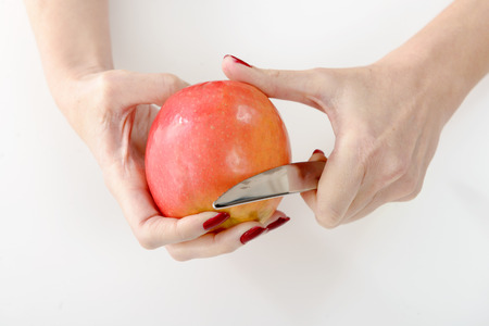 Hands of young woman peeling an apple, isolated on whiteの写真素材