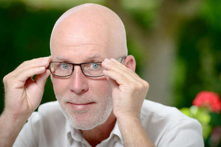 a portrait of a mature man with glasses near a windowの写真素材