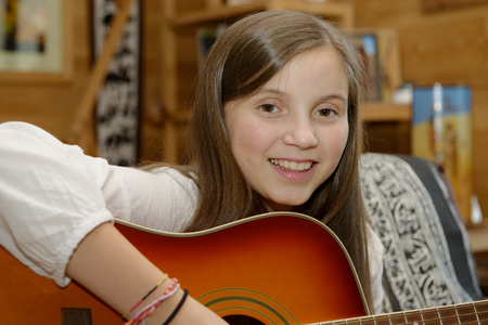 Young teen girl playing acoustic guitar on sofaの写真素材