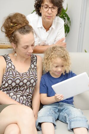 a child and his mother and his grandmother play with tablet