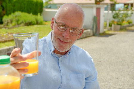 a senior man drinking  orange juice in her gardenの写真素材