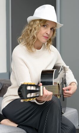 beautiful young blonde woman with hat playing the acoustic guitarの写真素材