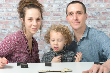 happy family mother, father and child playing dominos