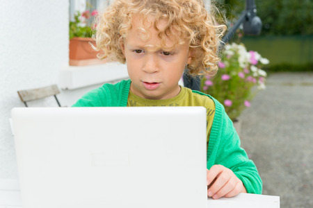 a portrait of a little blond boy using a laptopの写真素材