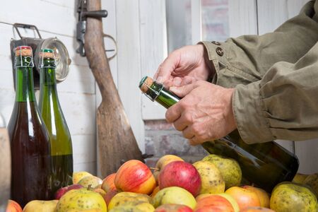 a man opening bottle of cider, apples on tableの写真素材