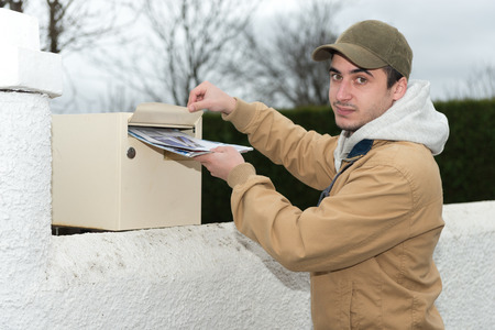 young man putting newspaper from the mailboxの写真素材