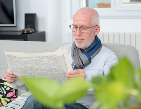 handsome mature man reading a newpaper on sofaの写真素材