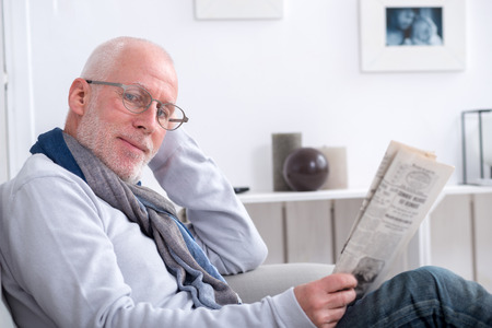 handsome mature man reading a newpaper on sofaの写真素材