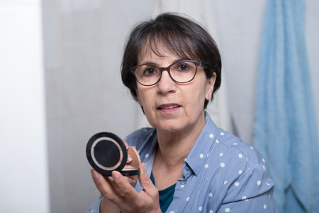 mature woman doing makeup while looking at a small mirrorの写真素材