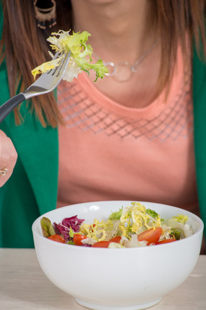 a brunette woman with green jacket, eating salad の写真素材