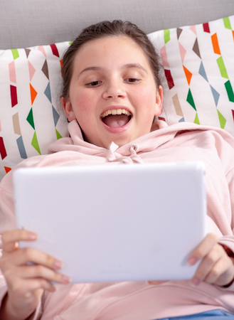 a smiling teenage girl playing with tablet at home