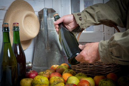 a close up of man hands with a bottle of cider and applesの写真素材