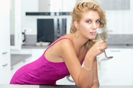 beautiful young blonde woman with a pink dress drinks a glass of white wineの写真素材