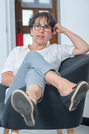beautiful brunette mature woman sitting in an armchair at homeの写真素材