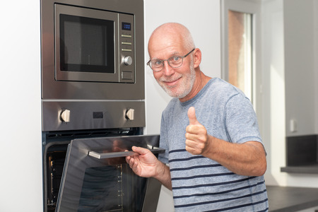 a mature man putting the meal in the ovenの写真素材