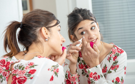 a young brunette woman putting makeup in the mirror