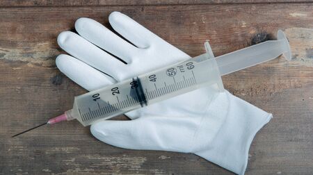 white gloves with a big syringe on wooden backgroundの写真素材