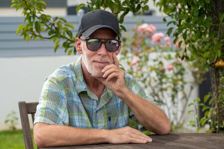 senior man in a baseball cap with sunglasses relaxing in the garden