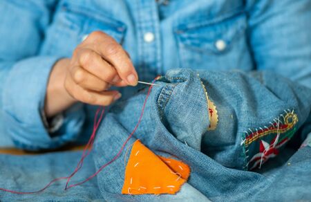 an elderly woman hands sewing on fabric jeans, needle.