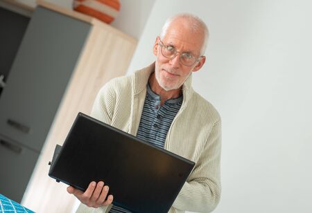 Senior with grey hairs wearing eyeglasses holding a laptopの写真素材