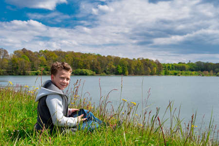 a smiling boy sitting near the lakeの写真素材