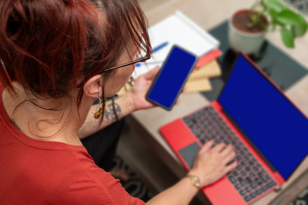 a young woman uses her phone and laptop at homeの写真素材