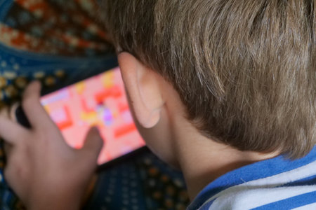 A boy is playing a game on his phone. The game is colorful and has a maze-like designの写真素材