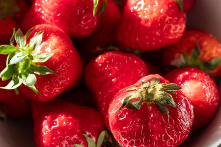 A bowl of red strawberries with green leaves. The strawberries are ripe and ready to eat. The bowl is white and the strawberries are the main focus of the imageの写真素材