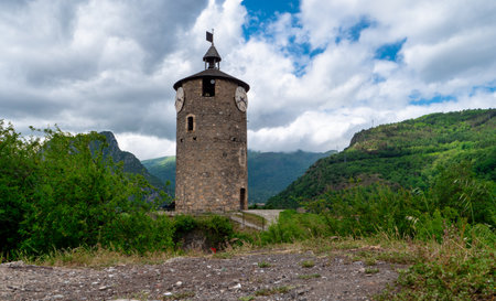 Tarascon sur Ariege, France, the tall tower with a clock. The sky is cloudy and the mountains in the background are greenの写真素材